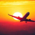 Avião decolando em direção a um pôr do sol vibrante.