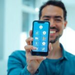 Pessoa sorrindo com celular e ícones financeiros digitais.
